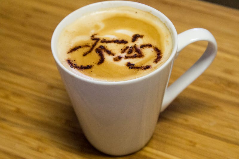 A coffee mug with coffee and foamed milk shaped into the design of a bicycle.